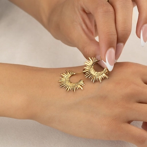 Detailed view of golden sunburst C-shaped earrings with textured metallic finish