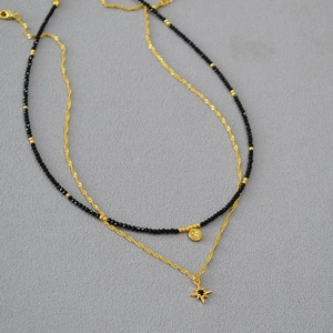 Detail of double-layer necklace featuring black faceted beads and gold star pendants
