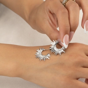 Close-up of silver geometric semi-circle earrings with sunburst ray texture detail