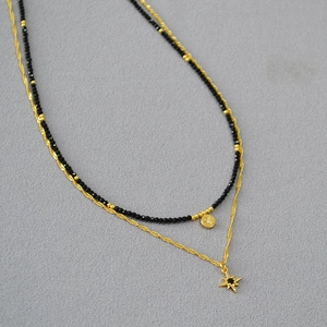Detailed macro view of double-layered gold chain necklace with black spinel beads and star pendants