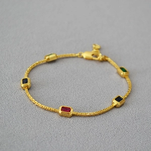 Close-up of gold chain necklace with colorful rectangular gemstones and woven texture