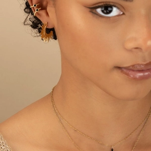 Close-up of golden sunburst earring with black stone studs and layered chain set