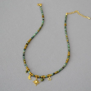 Retro turquoise beaded necklace with gold moon and star charms on textured fabric