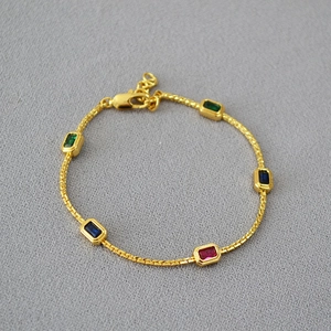 Gold chain necklace with five rectangular colored gemstones on a grey textured background