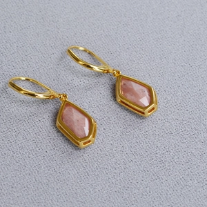 Detailed view of long geometric earrings with faceted pink natural gemstones and gold finish
