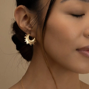 Close-up of a gold sunburst earring featuring geometric radiant lines on a model