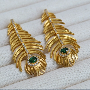Vintage gold feather earrings with green emerald stones and zircon accents on beige velvet