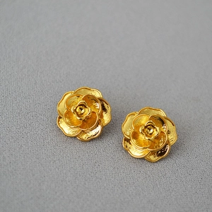Détail macro de boucles d'oreilles camélia 3D dorées à la finition mate sur tissu sombre