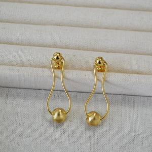 Detail of gold drop earrings featuring a brushed texture sphere and elegant curved lines