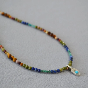 Gros plan d'un pendentif flèche turquoise et d'un collier de perles colorées à facettes