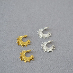 Close-up of gold and silver sunburst half-circle earrings with hammer texture