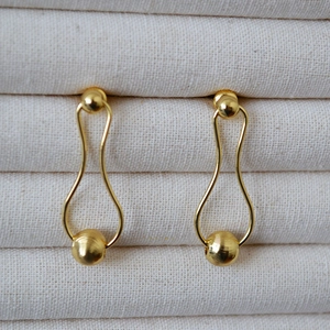 Detail of elegant gold-plated drop earrings with textured metal beads in a jewelry box