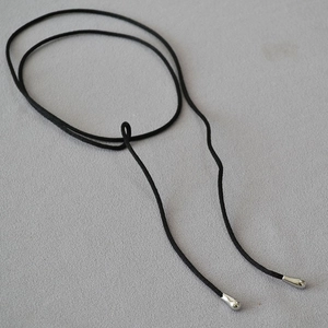 Detailed view of long black cord choker with silver teardrop pendants on grey fabric