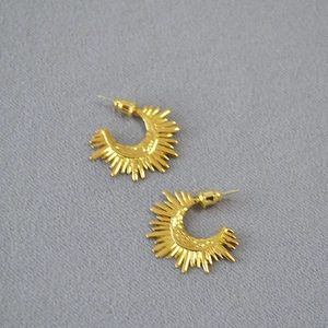 Detail shot of golden sunburst C-shaped earrings with radial geometric rays on grey fabric