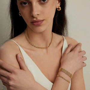 Detail of chunky gold plated chain bracelet and bangle set worn by a fashion model