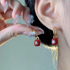 Gros plan de boucles d'oreilles créoles dorées avec pendentifs carrés en émail rouge