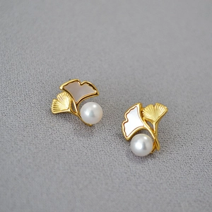 Macro view of gold-plated ginkgo leaf earrings with white pearl and brushed texture