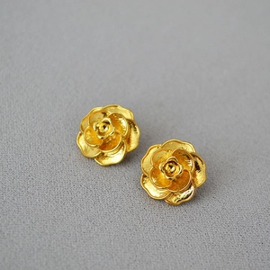 Boucles d'oreilles camélia doré avec pétales texturés sur fond gris épuré