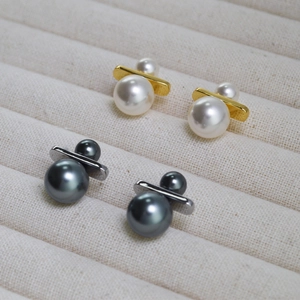 Macro view of minimalist double pearl earrings in gold and silver finishes on velvet tray
