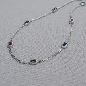Macro shot of colorful rectangular gemstones set in a polished silver braided chain necklace