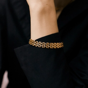 Golden mesh link bracelet with watch strap design on a dark fabric background