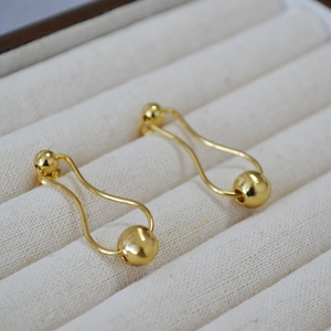 Detail of gold-plated brass earrings with a brushed spherical bead on white velvet