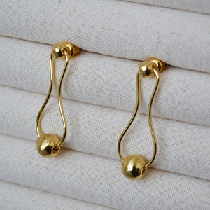 Detailed close-up of gold-plated brass drop earrings with minimalist curved lines