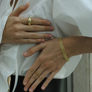 Detailed view of women wearing gold watchband chain bracelet and stacked rings