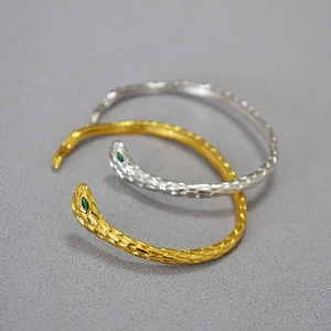 Dettaglio di anelli a serpente oro e argento con occhi in gemma verde e squame