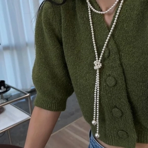 Gros plan d'un long collier de perles noué porté sur un gilet en maille vert élégant