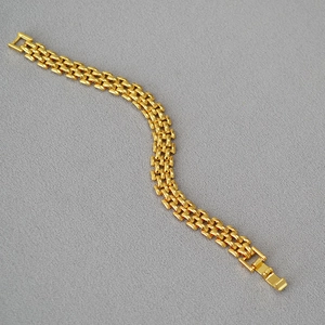 Macro detail of golden metal watch-style link bracelet with a polished folding clasp