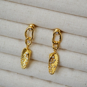 Irregular leaf-textured gold earrings with pearls and zircon on a beige fabric background