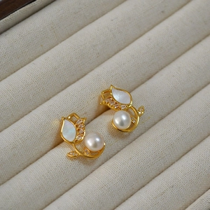 Detailed close-up of golden tulip stud earrings with white pearls in a jewelry box