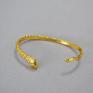 Bracciale a serpente aperto in oro con occhi di pietre verdi e texture a scaglie fitta