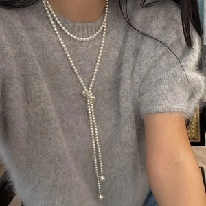 Détail d'un long collier de perles à double rangée avec pendentif nœud en Y sur pull
