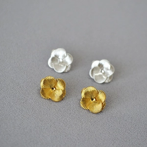 Dettaglio di orecchini a lobo a quadrifoglio oro e argento con texture metallica spazzolata