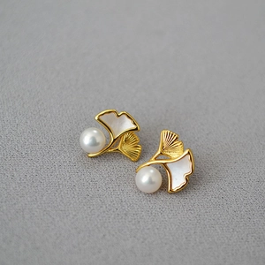 Detail of gold ginkgo leaf earrings with white inlay and glossy freshwater pearl