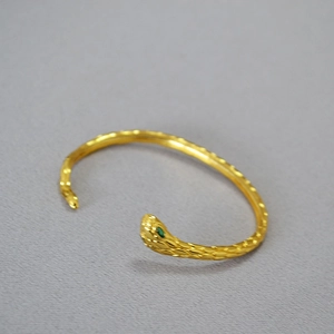 Dettaglio macro del bracciale a serpente dorato con occhio in gemma verde e squame