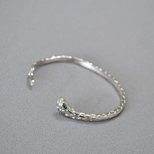 Dettaglio macro del bracciale a serpente argento con scaglie e occhi in gemma verde