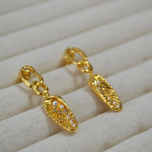 Gold wing earrings with pearls and zircon crystals on a beige velvet jewelry tray