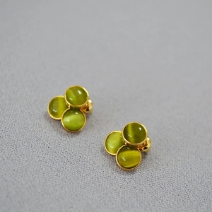 Macro detail of three-cluster green cat's eye stones in gold-plated stud earrings