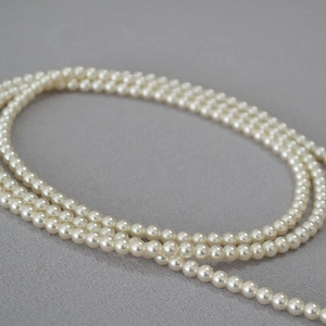 Détail macro d'un collier de perles crème élégant aux reflets doux sur tissu en maille gris