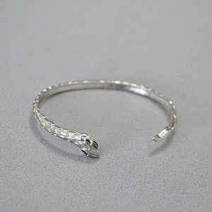 Dettaglio macro del bracciale a serpente in argento con occhi verdi e squame incise