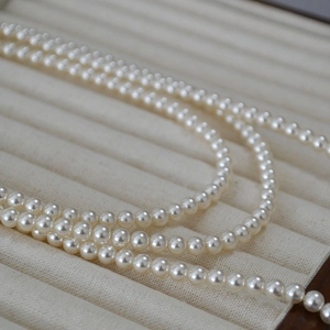 Collier long de perles nacrées élégant posé en courbe S sur un plateau bijoux