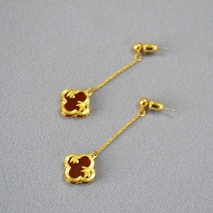 Detail of long gold clover earrings with red agate inlay on textured gray background