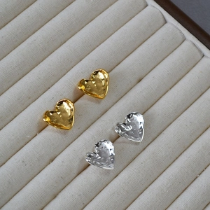 Minimalist hammered gold and silver heart stud earrings set on a beige jewelry display