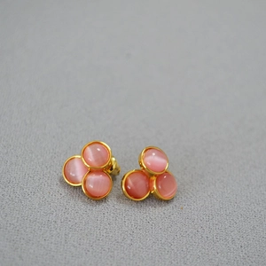 Detailed view of gold earrings with three pink cat-eye stones in a cluster design