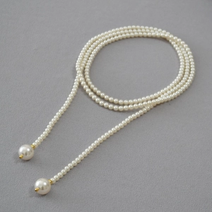 Détail d'un long collier lariat en perles avec touches dorées sur un fond gris texturé
