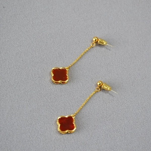Detail view of long gold earrings with red agate clover charm and 925 silver needles