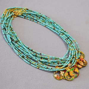 Détail d'un collier de perles turquoise multicouche avec pendentifs en émail doré